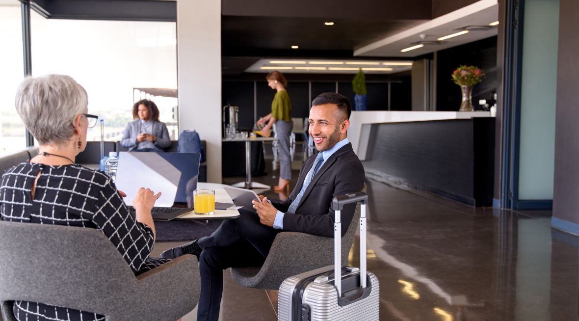 Diverse business partners sitting in modern airport lounge with baggage and computer smiling together